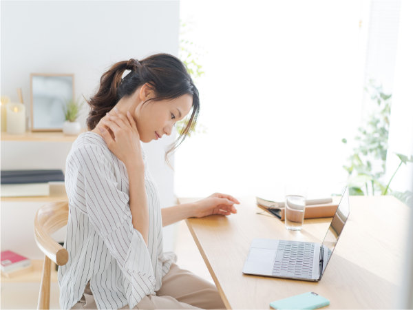パソコンを触りながら首を押さえる女性の写真